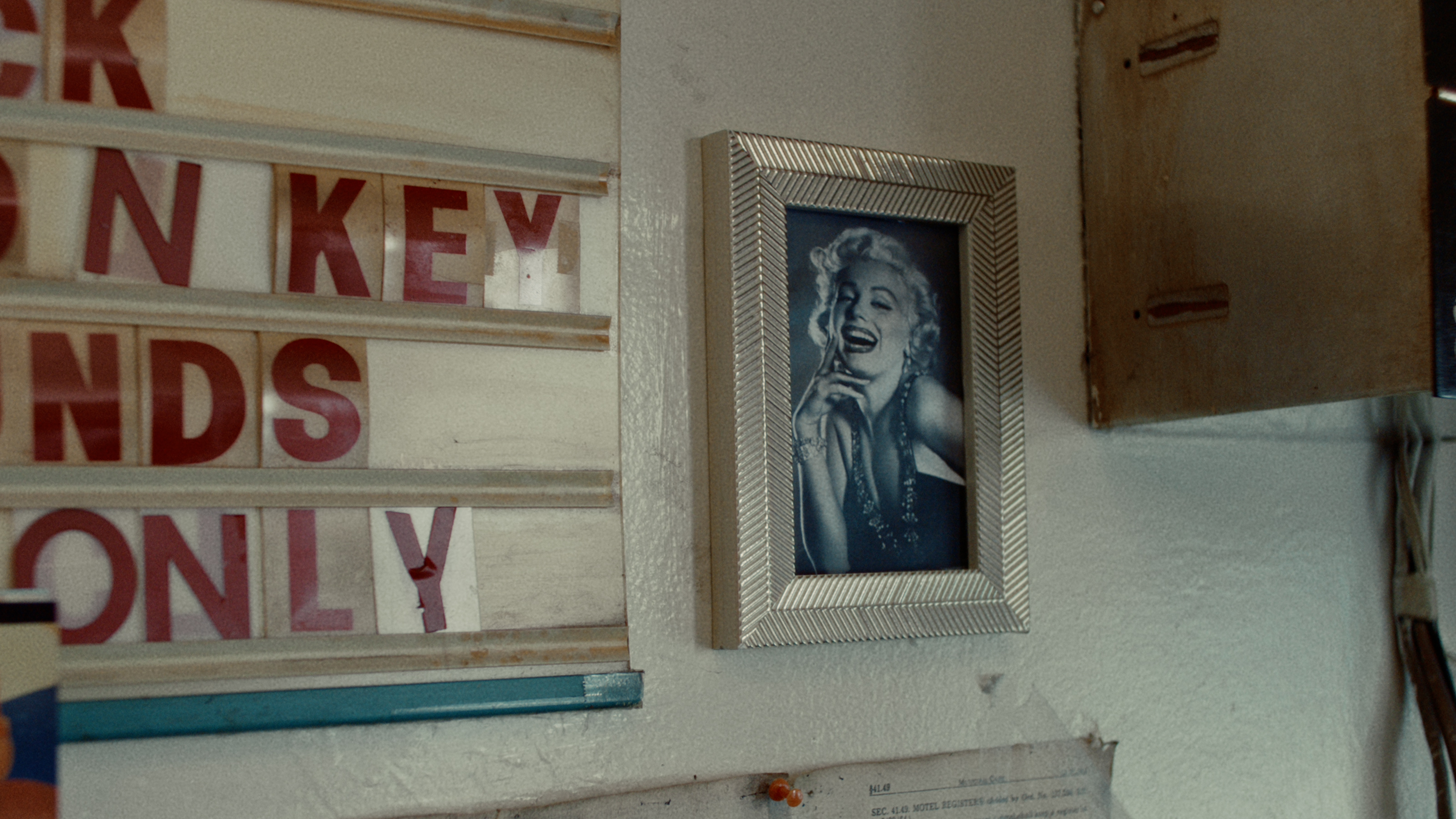 A framed Marilyn Monroe portrait hangs on a motel wall beside a letter board sign